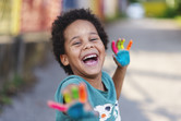 Photo of a child holding their hands up, covered in colorful paint.
