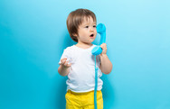 Photo of a toddler standing and holding an oversized throwback blue phone receiver. 