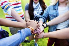 A group of youth put their hands together in show of unity and team work. 