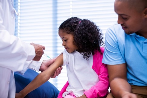 Young girl getting vaccine shot sitting next to father