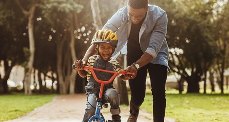 Father supporting sone on bike on a trail, laughing