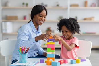 Day care teacher helping child play with blocks