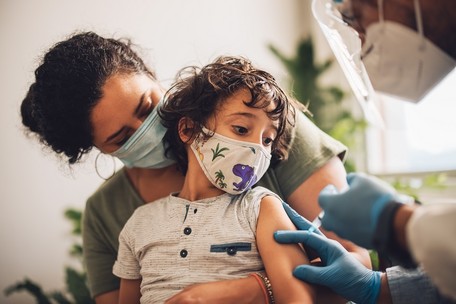 Young child sitting in mother's lap about to get a vaccine shot from a doctor