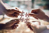 Photo of four hands, each holding one puzzle piece that all connect together