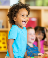 Preschoolers in a colorful classroom, smiling and interacting in a small group.