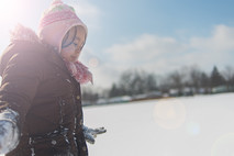 Photo of a child bundled up, walking in the snow on a sunny day.