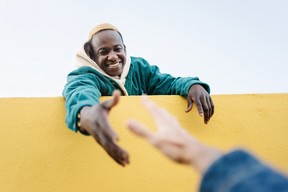 Young man extending a hand to help someone over a wall