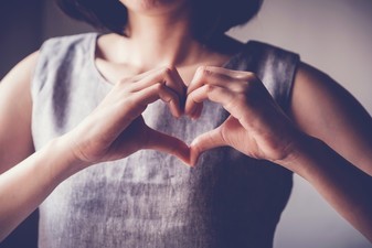 Woman holding hands in heart shape in front of her actual heart