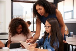 Black woman teacher helping two teenage girls, both BIPOC.