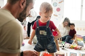 Caregivers and toddlers play with toys in a brightly lit playroom.