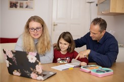 mom and dad sitting with daughter in front of a laptop screen