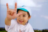 Photo of a young Asian child with his arm outstretched toward the camera, signing "I LOVE YOU" with one hand.
