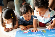 Three toddlers intently look at colorfully illustrated books.
