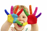A laughing child holds their hands up, covered in colorful paint.