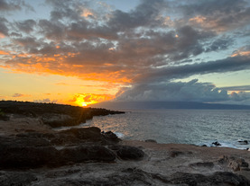 photo of a hawaiin beach with clouds and a sunset off to the left side 