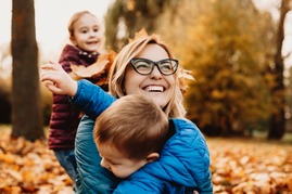 woman with glasses playing in pile of leaves with two young children