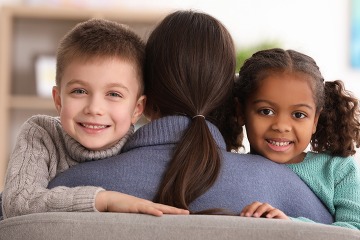 two young kids hugging their mom while smiling and looking into the camera 