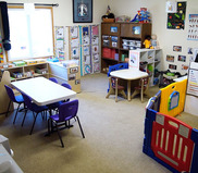 Neat and tidy child care classroom with two desks and pictures on walls and book shelves.
