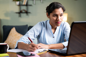 woman looking at laptop while taking notes