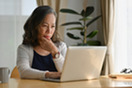 Medium shot of a middle-aged woman concentrating, looking intently at a laptop.