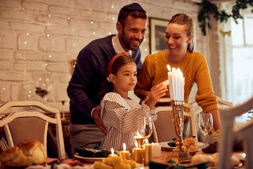 a dad, mom and young child lighting a menorah at the dining table