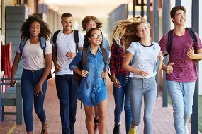 kids smiling with backpacks walking down school hallway
