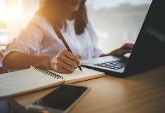 women at laptop writing notes in notepad