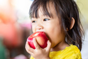 Young girl of color with dark hair taking a big bite out of a juicy apple.