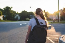 Picture of sad teenage girl wearing backpack and shorts walking away from camera
