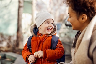 Caregiver laughing with kindergarten child in the schoolyard.