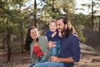 mom and dad smiling with baby with trees in background