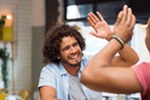 man with brown curly hair smiling and high fiving friend