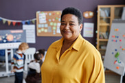 Woman of color stands proud in child care center classroom.