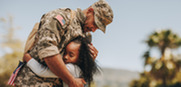 Young girl of color embraces father in military fatigues.