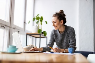 women smiling at the computer with coffee and plant in background