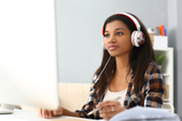 Woman of color sitting at desk with headphones on at computer.