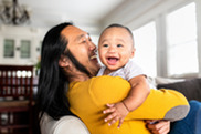 Man with dark long hair holding infant, both with big smiles.