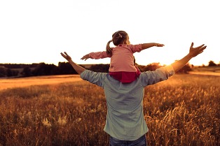 daughter sitting on dads shoulder looking across a wheat field