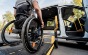 photo of a back of a man on a wheelchair that's getting loaded on a van. 