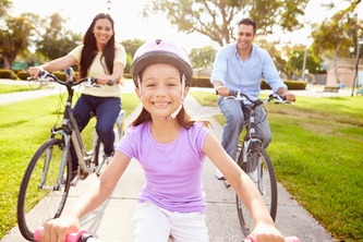 Parents With Daughter Riding Bikes In Park