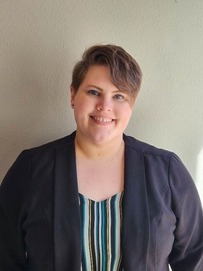 Medium shot of Jaclyn Johnson, wearing a gray blazer, striped blouse and smiling for the camera.