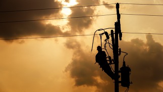 The silhouette of power lineman climbing on an electric pole with a transformer installed