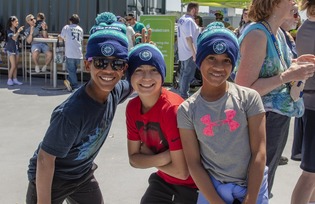 Three kids smiling at the camera with mariner beanies on