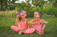 Young girls sit on grass in pink outfits holding artistic colorful hearts.