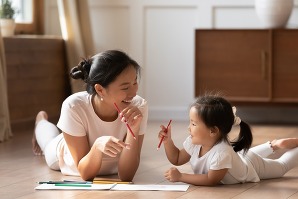  Asian mother her small daughter lying on warm wooden floor in sunny cozy living room