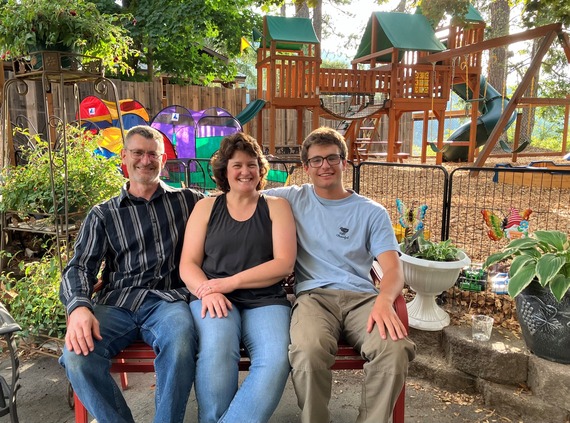 Two men and one woman sit in park bench with playground behind them on nice sunny day.