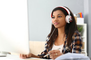 Woman of color sits at computer wearing headphones.