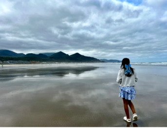 girl walking on a beach wearing a dress and a bow in her hair 