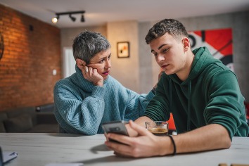 teenage boy and mature white woman sit together at the kitchen