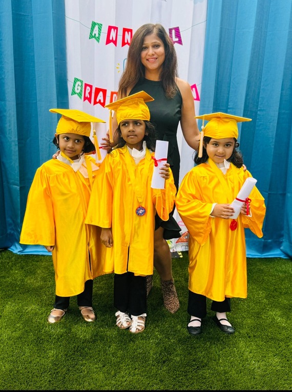 Woman of color with dark hair stands with three children in yellow cap and gowns.